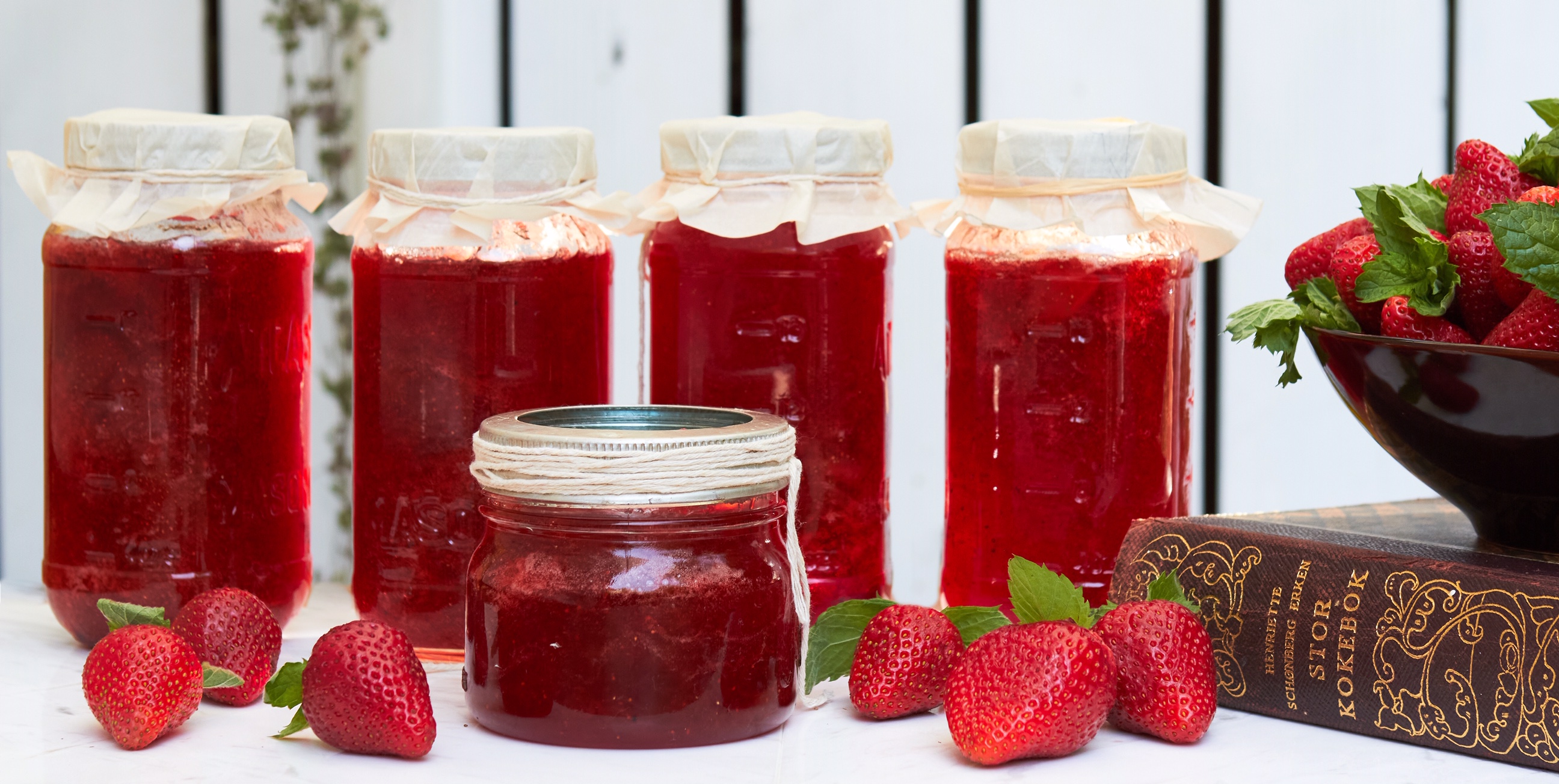 Strawberry jam jars in a row, some with fresh strawberries beside them